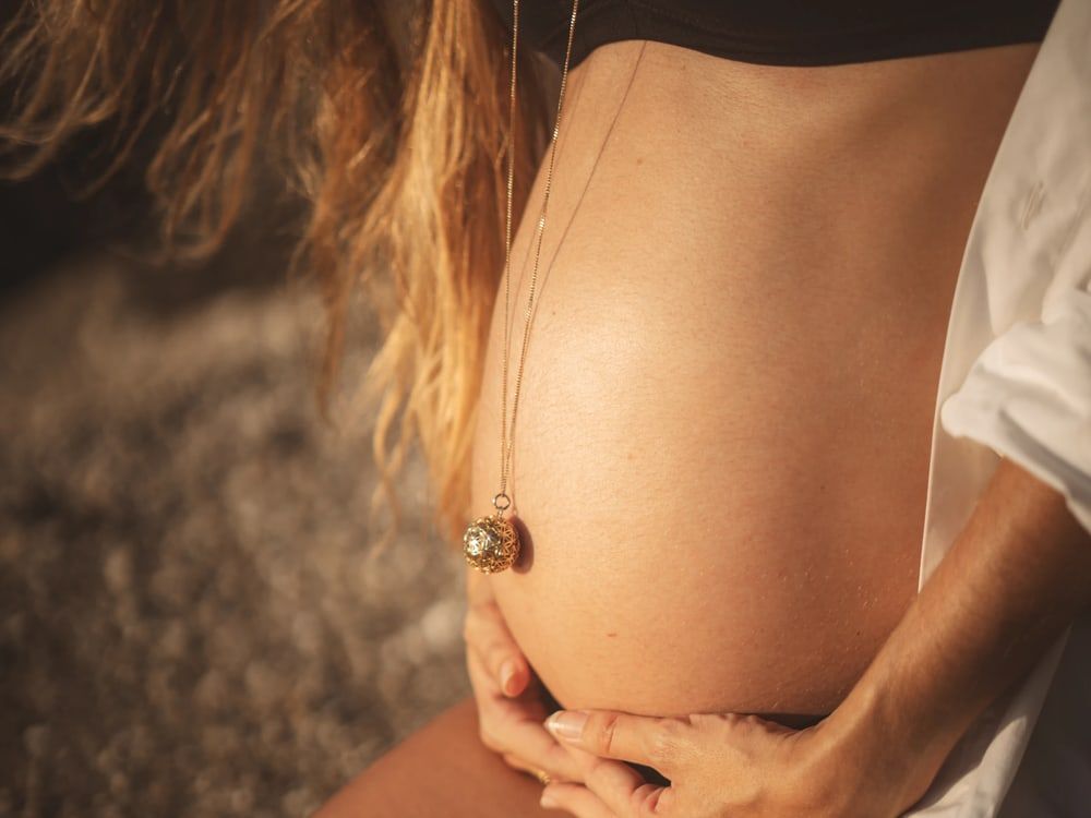 Ventre arrondi d’une femme enceinte, ses mains posées dessous, dans une lumière chaude de fin de journée