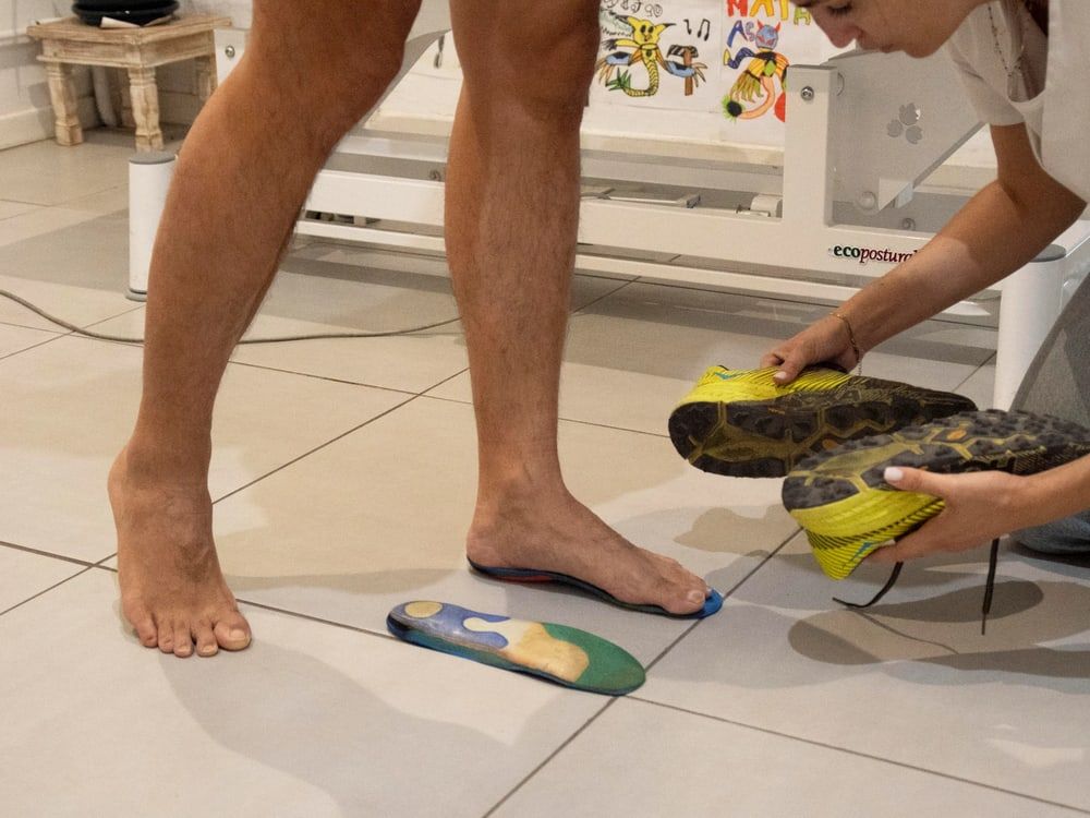 Observation d’un pied posé sur une semelle, pendant que l’ostéopathe examine une paire de chaussures de trail